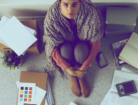 Young female fashion designer working at office desk, drawing while talking on mobileの写真素材