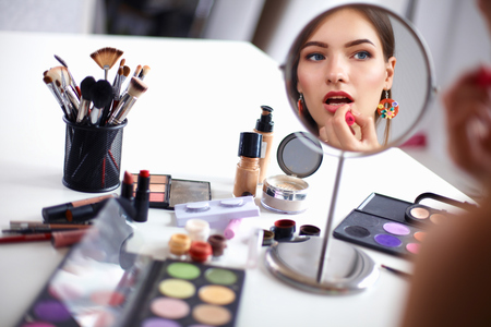 Young beautiful woman making make-up near mirror,sitting at the desk.の写真素材