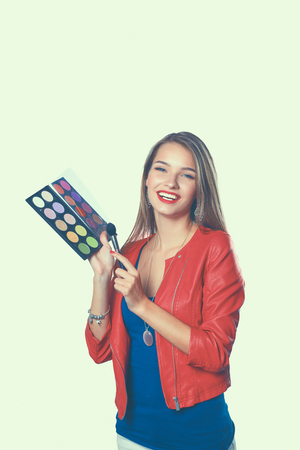 Young beautiful woman holds in one hand and a palette with paint and shadows for makeup, second hand brush for makeupの写真素材