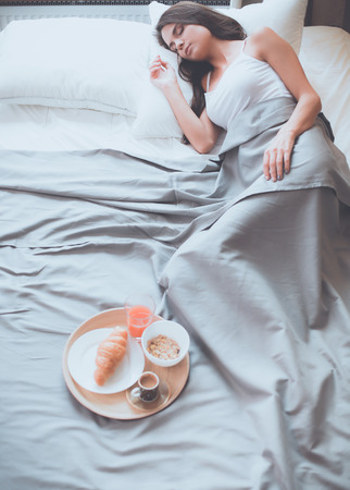 Young woman sitting in bed with a cup of milkの写真素材