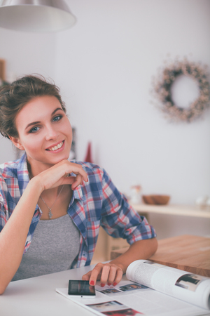 Portrait of young woman using mobile phone while having breakfast in kitchen at homeの写真素材