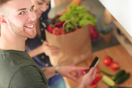 Happy couple using smartphone standing in kitchenの写真素材