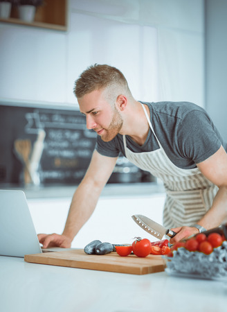 Portrait of man cooking vegetable in the kitchen while looking at a laptop computer on the tableの写真素材