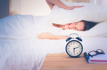 A young woman putting her alarm clock off in the morning.の写真素材