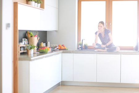 Young beautiful woman sitting at the kitchen table in the lotus positionの写真素材
