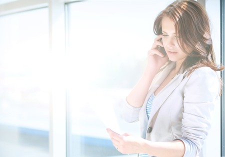 Portrait of young businesswoman talking on mobile phone in office hallwayの写真素材