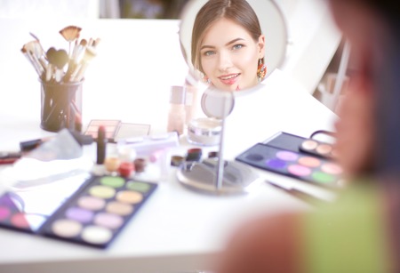 Young beautiful woman making make-up near mirror,sitting at the deskの写真素材