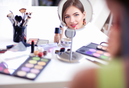 Young beautiful woman making make-up near mirror,sitting at the deskの写真素材