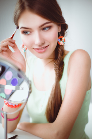 Young beautiful woman making make-up near mirror,sitting at the deskの写真素材