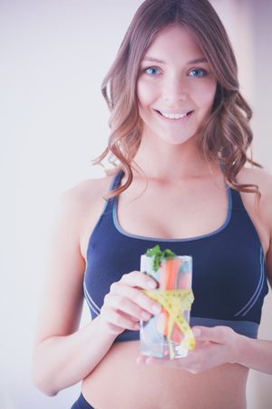 Woman holding a drinking glass full of fresh fruit salad with a tape measure around the glass.の写真素材
