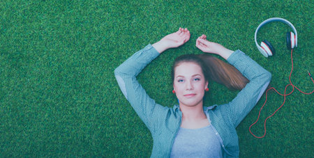 Relaxed woman listening to the music with headphones lying on grass