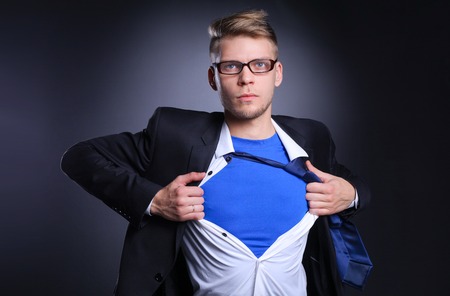 Young businessman acting like a super hero and tearing his shirt, isolated on gray background. Young businessmanの写真素材