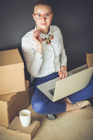 Woman sitting on the floor near a boxes with laptop . Businesswomanの写真素材