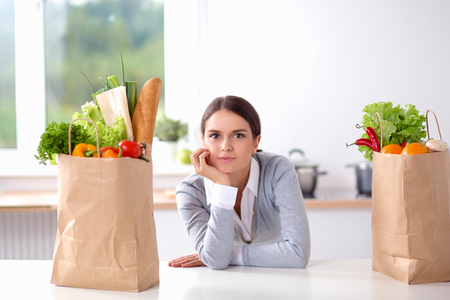 Young woman holding grocery shopping bag with vegetables . Standing in the kitchenの写真素材