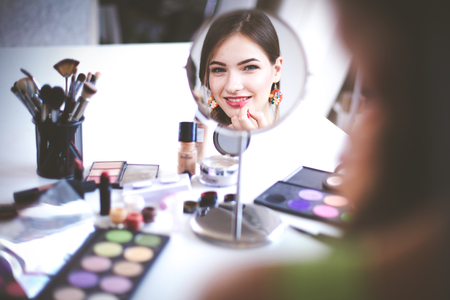 Young beautiful woman making make-up near mirror,sitting at the deskの写真素材
