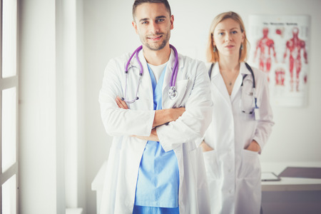 Handsome doctor is talking with young female patient and making notes while sitting in his officeの写真素材