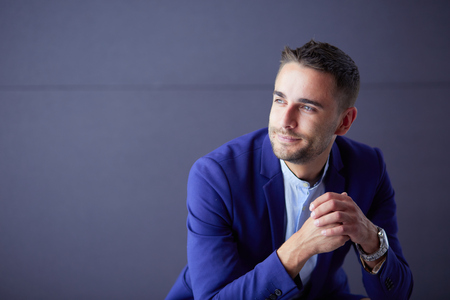 Young businessman sitting isolated on grey backgroundの写真素材