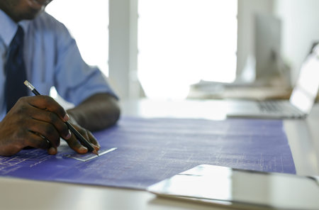 African american architect working with computer and blueprints in office.