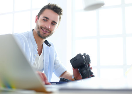 Portrait of young designer sitting at graphic studio in front of laptop and computer while working...