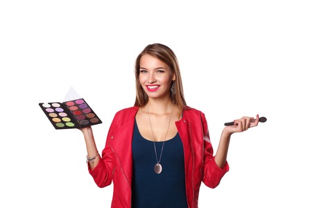 Young beautiful woman holds in one hand and a palette with paint and shadows for makeup, second hand brush for makeup.の写真素材