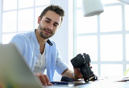 Portrait of young designer sitting at graphic studio in front of laptop and computer while working online.の写真素材