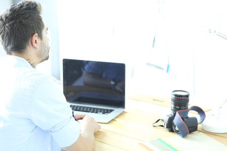 Portrait of young designer sitting at graphic studio in front of laptop and computer while working...