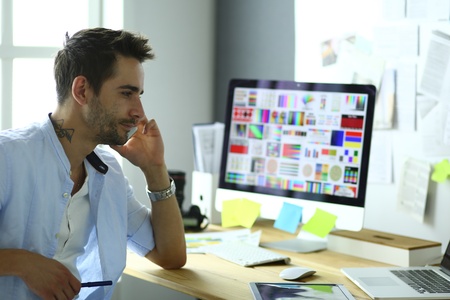 Portrait of young designer sitting at graphic studio in front of laptop and computer while working online.の写真素材