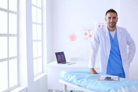Portrait of a male doctor with laptop sitting at desk in medical office.の写真素材