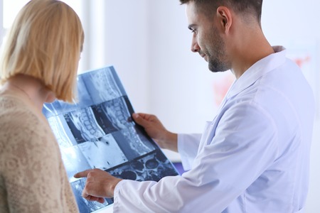 Handsome doctor is talking with young female patient and making notes while sitting in his office.の写真素材
