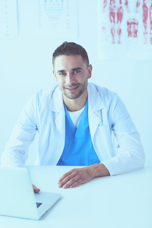 Portrait of a male doctor with laptop sitting at desk in medical office.の写真素材
