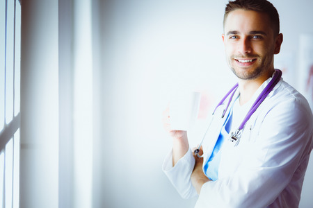 Young doctor with coffee cup in medical officeの写真素材
