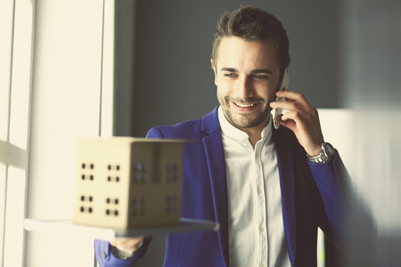 Businessman holding house miniature on hand standing in office.の写真素材