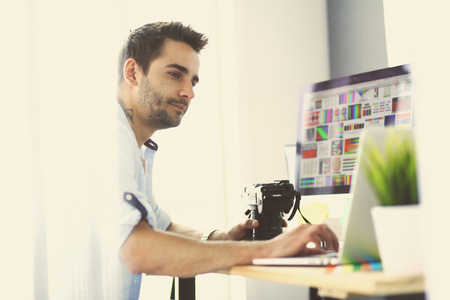 Portrait of young designer sitting at graphic studio in front of laptop and computer while working online.の写真素材