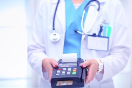 Doctor is holding payment terminal in hands. Paying for health care. Doctorの写真素材