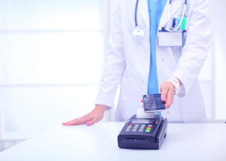 Doctor is holding payment terminal in hands. Paying for health care. Doctorの写真素材