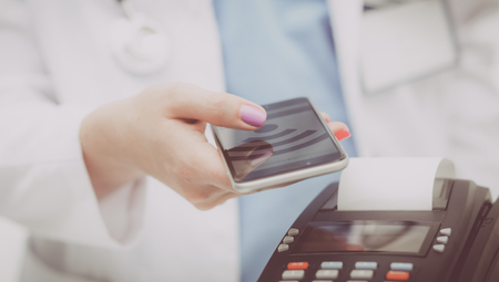 Doctor is holding payment terminal in hands. Paying for health care. Doctorの写真素材