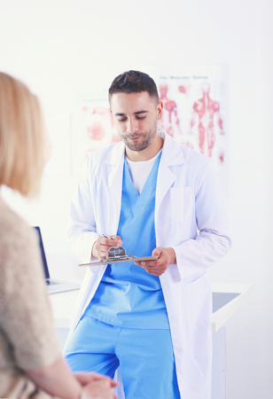 Handsome doctor is talking with young female patient and making notes while sitting in his office.の写真素材