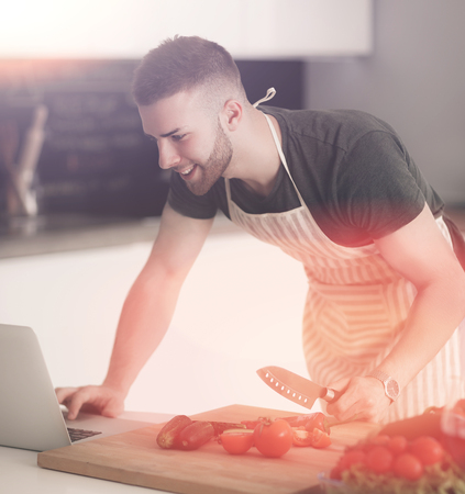 Portrait of man cooking vegetable in the kitchen while looking at a laptop computer on the tableの写真素材