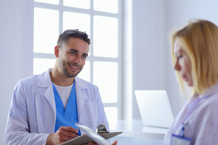 Handsome doctor is talking with young female doctor and making notes while sitting in his office.の写真素材
