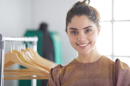 Beautiful young stylist near rack with hangersの写真素材