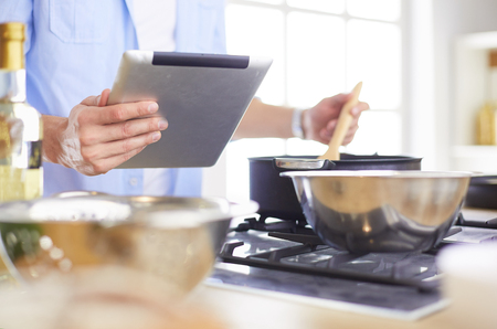 Man following recipe on digital tablet and cooking tasty and healthy food in kitchen at homeの写真素材