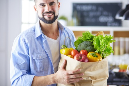 Man holding paper bag full of groceries on the kitchen background. Shopping and healthy food conceptの写真素材