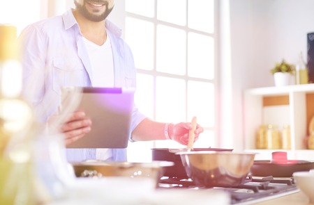 Man following recipe on digital tablet and cooking tasty and healthy food in kitchen at homeの写真素材