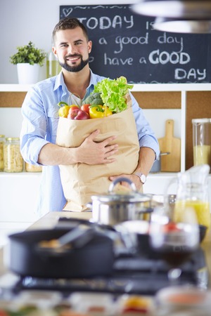 Man holding paper bag full of groceries on the kitchen background. Shopping and healthy food conceptの写真素材