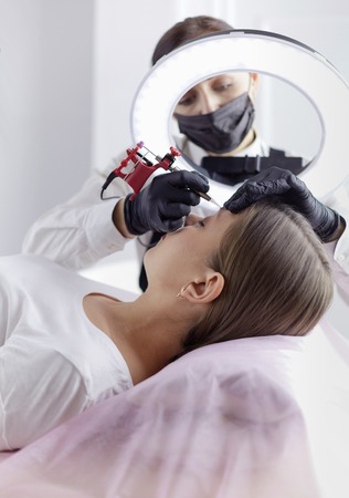 Microblading eyebrows work flow in a beauty salon. Woman having her eye brows tintedの写真素材