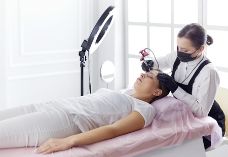 Microblading eyebrows work flow in a beauty salon. Woman having her eye brows tintedの写真素材