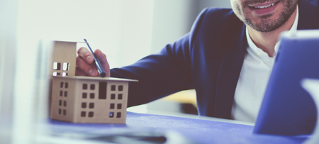 Businessman holding house miniature on hand standing in office.の写真素材