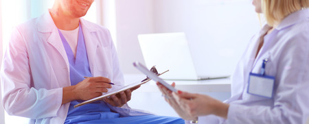 Handsome doctor is talking with young female patient and making notes while sitting in his officeの写真素材