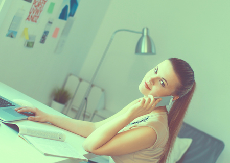 Young businesswoman sitting at the desk and talking on phoneの写真素材