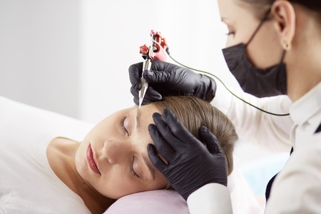 Young woman undergoing procedure of eyebrow permanent makeup in beauty salonの写真素材